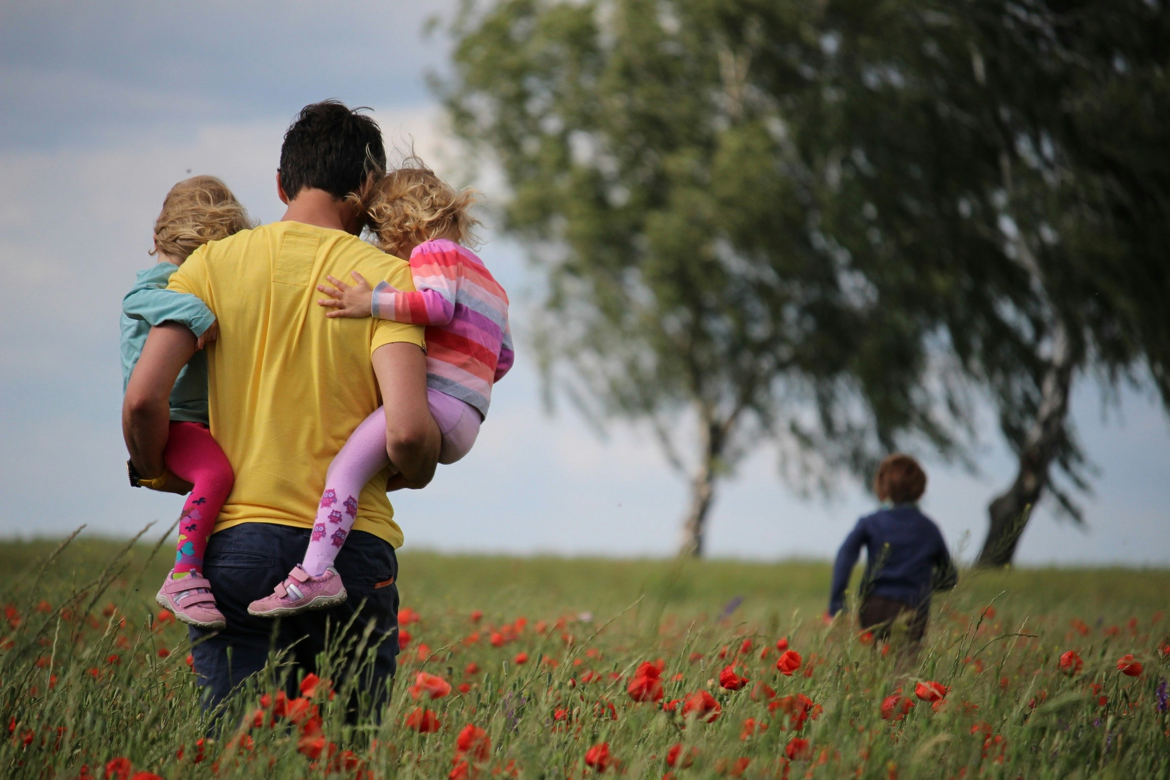 Ein Vater trägt zwei Kinder durch ein Mohnfeld, ein drittes Kind läuft voraus