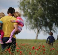 Ein Vater trägt zwei Kinder durch ein Mohnfeld, ein drittes Kind läuft voraus