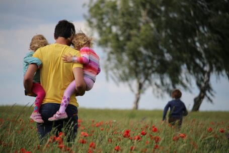 Ein Vater trägt zwei Kinder durch ein Mohnfeld, ein drittes Kind läuft voraus